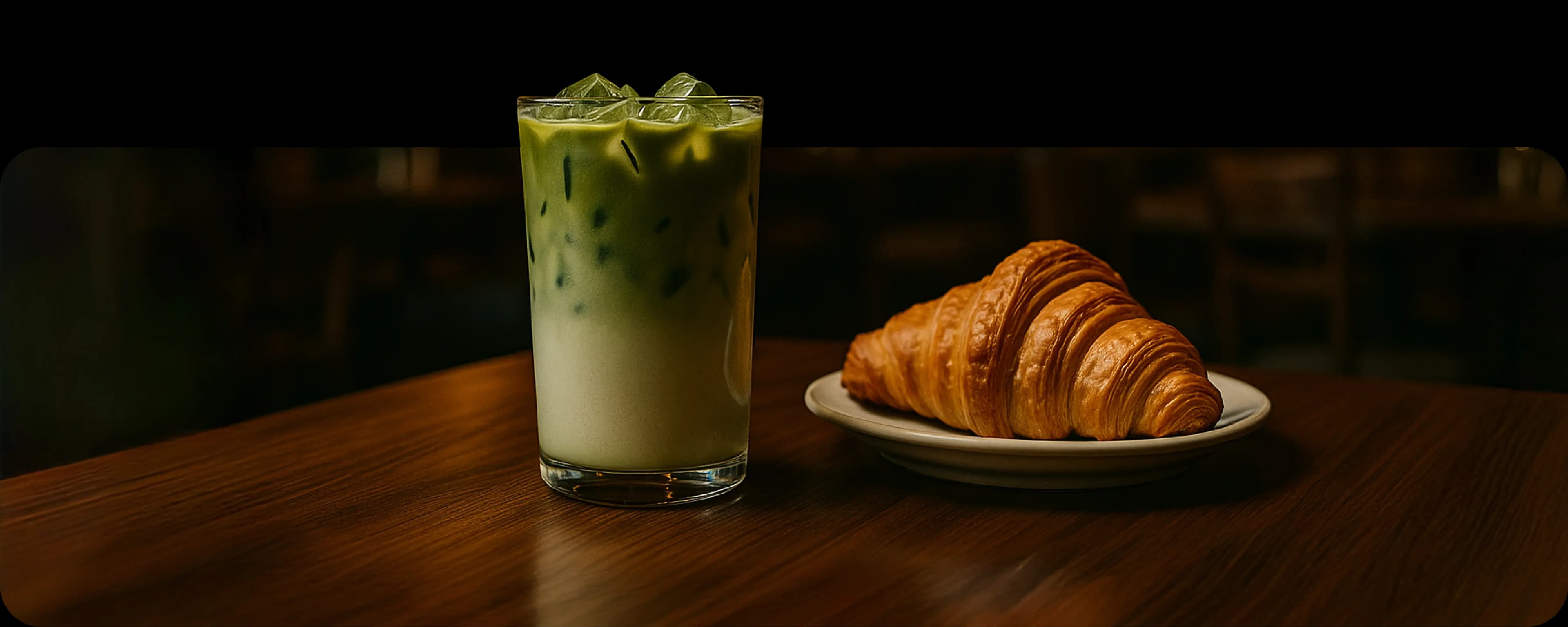 Рука держит ложку, из которой стекает соус на изысканно сервированное блюдо на тарелке, на фоне приглушённого интерьера и человека в белой рубашке.