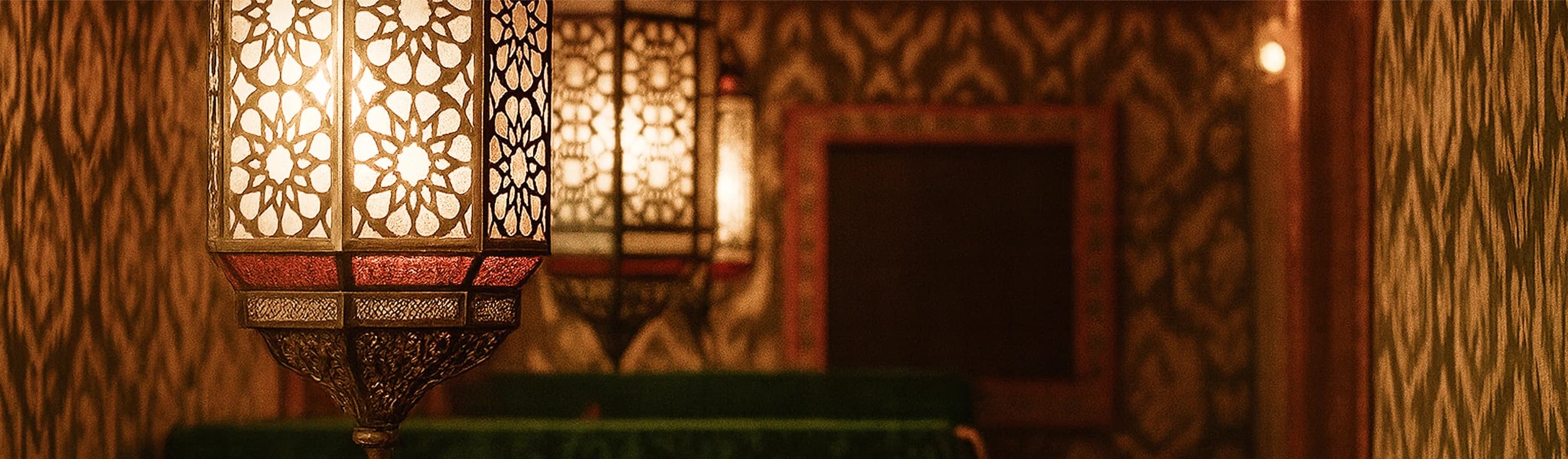 Мужчина и женщина сидят бок о бок за столом на мягкой скамье: оба улыбаясь смотрят на экран смартфона, который держит женщина; на заднем плане — ярко-красная стена и часть интерьера заведения.